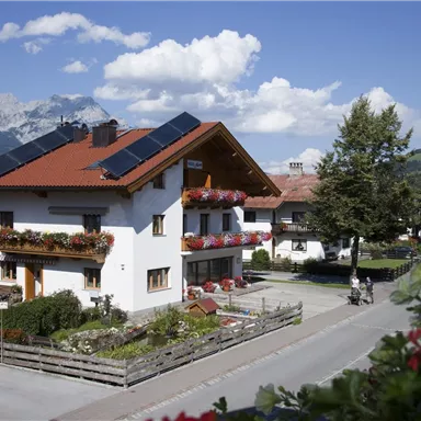 A beautiful house with flower boxes and solar panels. In the background, mountains and a clear sky are visible.