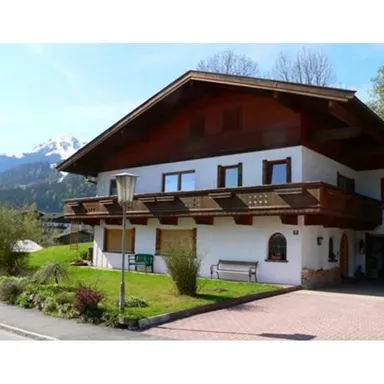 A cozy house in alpine style with a large garden. In the background, the mountains and a clear sky can be seen.