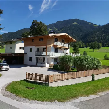 Ein schönes Haus in den Bergen mit einem gepflegten Garten. Im Hintergrund sind grüne Wiesen und Bäume zu sehen.