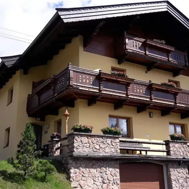 A cozy chalet-style house with wooden balustrades and a well-maintained garden. The facade is painted in warm yellow tones and radiates an inviting atmosphere.