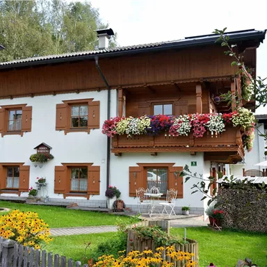 A beautiful, traditional house with flower balconies and a well-maintained garden. The building has a rustic wooden façade and is located in a quiet environment.