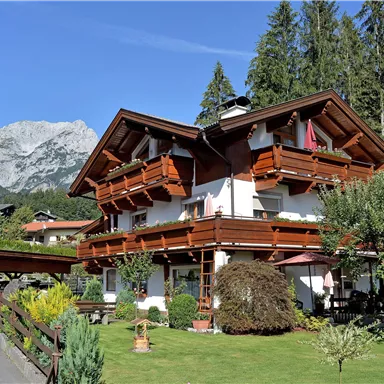 Ein charmantes Haus im alpine Stil mit Fenstern und Balkonen. Umgeben von Bäumen und Bergen in einer schönen Naturlandschaft.