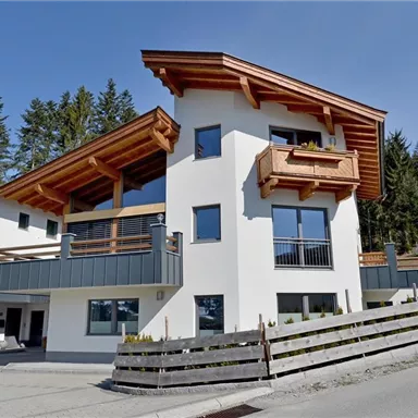 Ein modernes Haus mit Holzdetails und großen Fenstern in einer ruhigen Umgebung. Die umliegenden Bäume und die Straße verleihen der Szene eine charmante Atmosphäre.