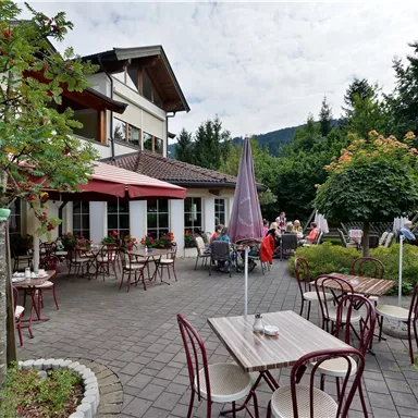 An inviting restaurant with outdoor seating and umbrellas. The surroundings are green and idyllic, ideal for relaxing.