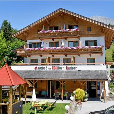 Ein einladendes Gasthaus aus Holz mit bunten Blumen auf dem Balkon. Umgeben von Bäumen und einer grünen Landschaft.