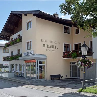 Ein charmantes Gästehaus mit Balkonen und Blumen dekoriert. Die Fassade ist hell und einladend, umgeben von Bäumen und einem ruhigen Straßenbild.