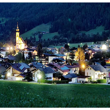 A picturesque village by night, surrounded by gentle hills. The church with its illuminated tower is an eye-catcher in the idyllic landscape.