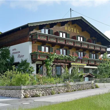 A traditional two to three-story hotel with a wooden facade and balconies. It is located surrounded by a green landscape and is decorated with plants.
