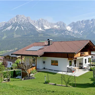 A picturesque landscape with a modern house and mountains in the background. The garden is green and inviting, ideal for a peaceful getaway.