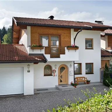 A modern single-family house with a brown gable roof. In front of the house, there is a paved path and a small garden.