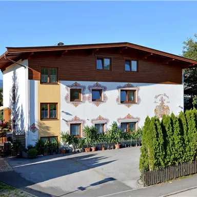 Ein traditionelles Haus mit einer schönen Fassade und mehreren Fenstern. Im Vordergrund befinden sich grüne Hecken und Pflanzen.