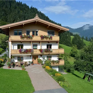 A beautiful building in alpine style, surrounded by green meadows and mountains. The house has balconies with flowers and a well-kept garden.