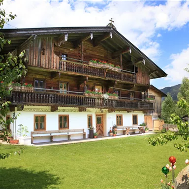 A traditional wooden house with multiple balconies in a green setting. The sky is blue with some clouds and the landscape is peaceful.