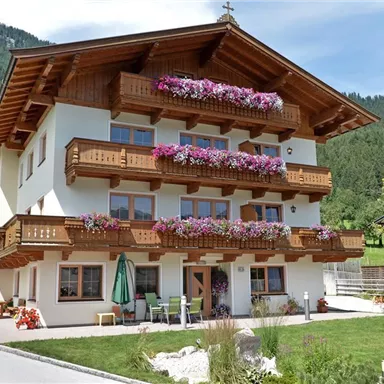 A traditional house with wooden balconies, adorned with colorful flowers.  
Surrounded by green mountains and a peaceful landscape.
