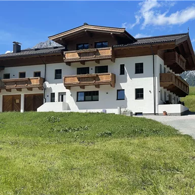 A modern building with several balconies and a clear blue sky in the background. The lawn in front is green and inviting.