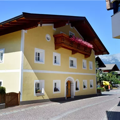 A charming yellow house with a balcony and flowers. The street is quiet and surrounded by typical architecture.