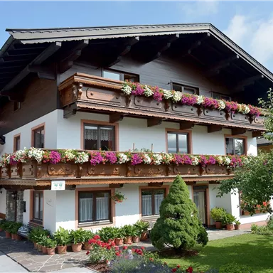 Ein schönes Gebäude im traditionellen Stil mit Blumen auf den Balkonen. Umgeben von gepflegten Gärten und einem klaren Himmel.