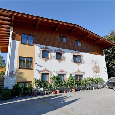 Ein charmantes zweistöckiges Gebäude mit einer bemalten Fassade. Vor dem Haus stehen viele Pflanzen und ein geparkter Wagen.
