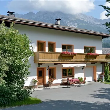 A charming house with a balcony and flower boxes. In the background, you can see mountains and a blue sky.