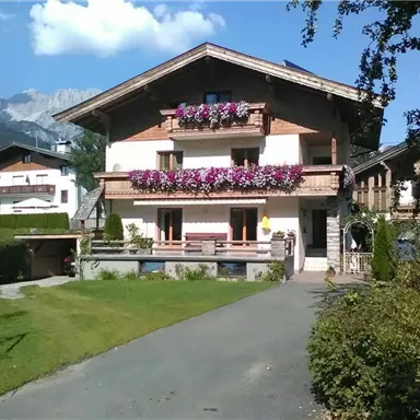 A charming house in the Alps with colorful flowers on the balcony. The well-maintained garden and the surrounding mountains create an idyllic atmosphere.