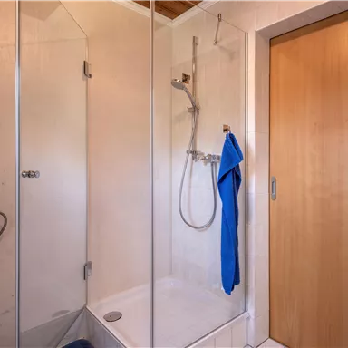 A modern bathroom with a shower cabin and a wooden chair. A blue towel is hanging on the shower.