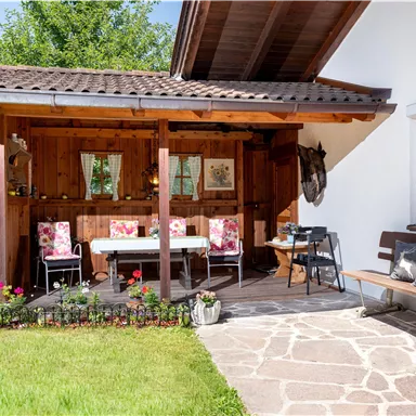 A cozy outdoor area with a wooden porch and colorful flowers. There is a table and chairs, ideal for relaxing outdoors.