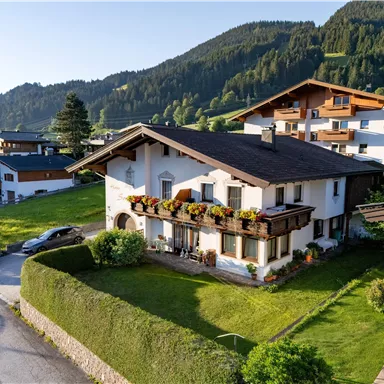 A beautiful house in the mountains with a well-maintained garden. In the background, green hills and forests can be seen.
