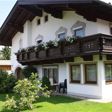 A beautiful house in alpine style with a balcony adorned with flowers. The well-kept garden and sunny surroundings create an inviting atmosphere.