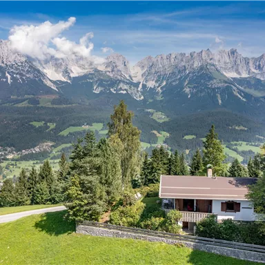 A cozy house in an idyllic landscape. In the background, majestic mountains rise under a clear sky.