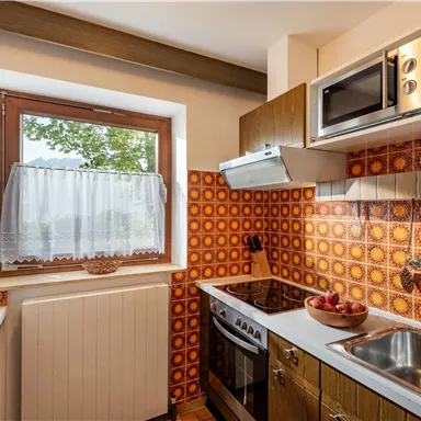 A bright kitchen with wooden cabinets and an orange tiled wall. It is equipped with modern appliances such as a microwave and a stove.
