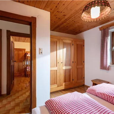 A cozy bedroom with two beds and wooden wardrobes. The windows let in plenty of daylight and create an inviting atmosphere.