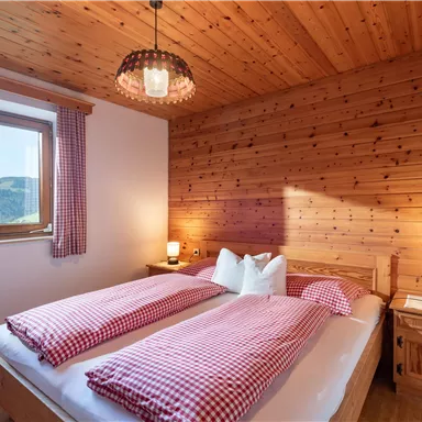 A cozy wooden bedroom with a window offering a view of the mountains. The two beds are decorated with checkered blankets and pillows.