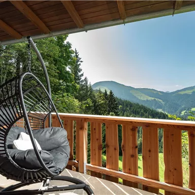 A rocking chair on a terrace overlooking green mountains. The sky is clear and sunny, perfect for relaxing.