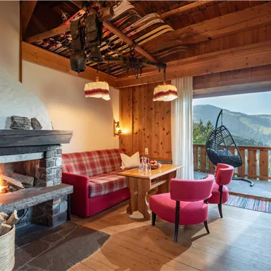 A cozy living space with wooden paneling and an open fireplace. Large windows provide a beautiful view of the mountains.