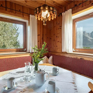 A cozy dining area with wood paneling and large windows. Coffee cups and a vase with fresh flowers are on the table.