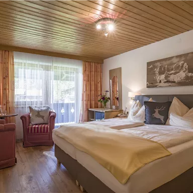 A cozy bedroom with a double bed and wood paneling. The room has large windows and a relaxing atmosphere.