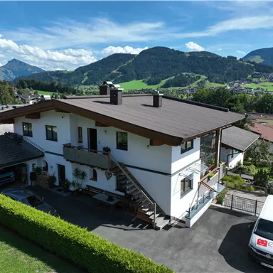 A modern house surrounded by green hills and mountains. The sky is blue with a few clouds.<br/>The house of the apartment and in the background the view towards Ellmau.