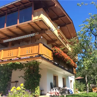 A charming house with a wooden balcony and blooming plants. The clear sky and green surroundings create an inviting atmosphere.