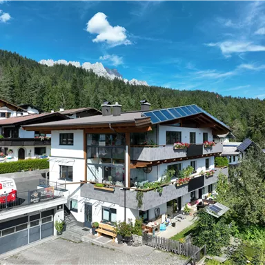 A modern building in the mountains surrounded by trees. The sky is clear and blue with a few clouds.