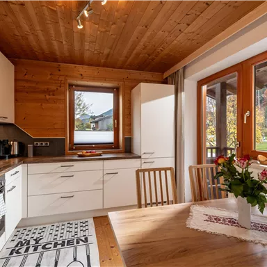 A modern kitchen with a wooden ceiling and white cabinets. A table with a bouquet of flowers invites you to linger.