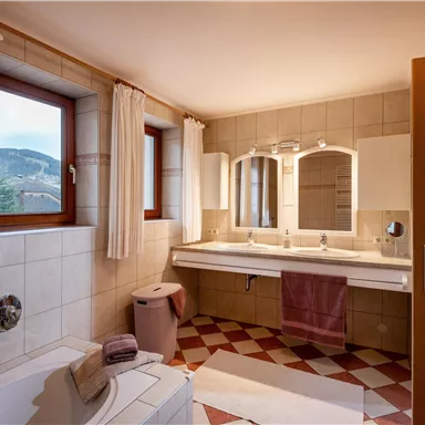 A modern bathroom with two sinks and large mirrors. Bright windows provide plenty of daylight and a pleasant atmosphere.