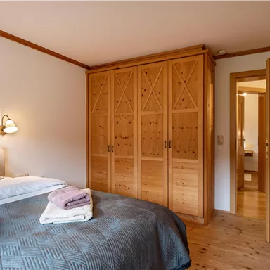A cozy bedroom with a large bed and a wooden wardrobe. The room has a warm, inviting atmosphere.