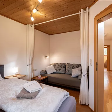 A cozy bedroom with a double bed and a sofa. The room is bright and modernly furnished, with wood paneling and warm lighting.