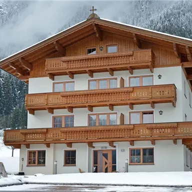 A charming mountain house with wooden balconies and alpine style, surrounded by snow-covered mountains. The quiet surroundings exude coziness.