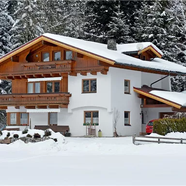 Ein schönes, winterliches Haus mit Holzverkleidung, umgeben von schneebedeckten Bäumen. Der schneebedeckte Garten und die ruhige Stimmung vermitteln eine gemütliche Atmosphäre.