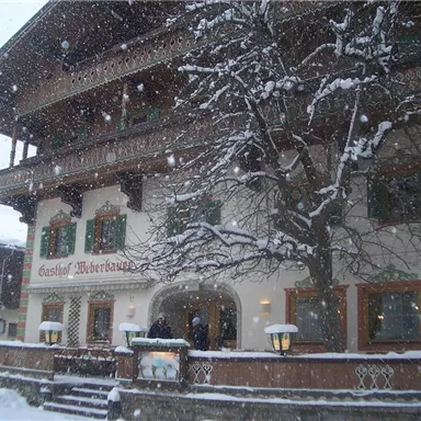 A traditional inn in the snow, surrounded by winter trees. Large snowflakes fall on the charming facade.