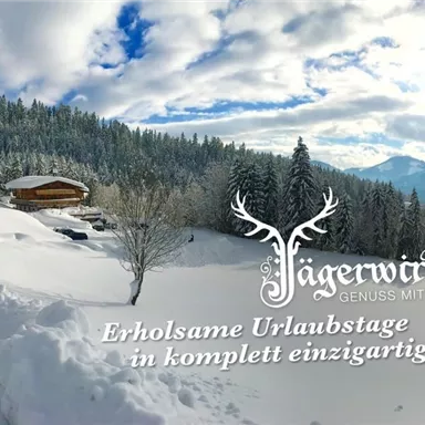 A wintry landscape with a lot of snow and a wooden house. The sky is partly cloudy and there are forests in the background.