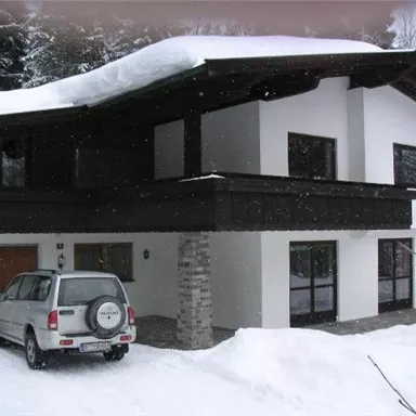 Ein modernes Haus im Schnee mit einem begrünten Dach. Ein Auto steht auf der Einfahrt vor dem Gebäude.
