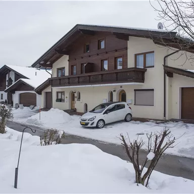 A modern house in the snow with a car in front of it. The surroundings are wintry and peaceful.