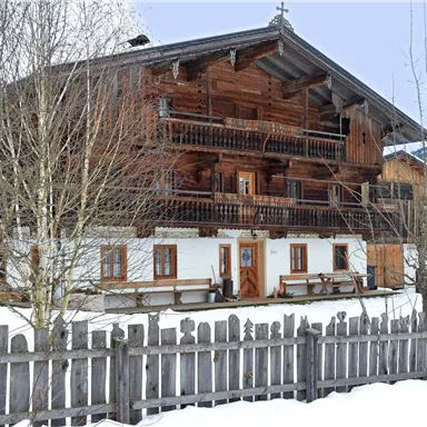 A traditional wooden chalet, surrounded by snow. The building has several balconies and a beautiful wooden fence.